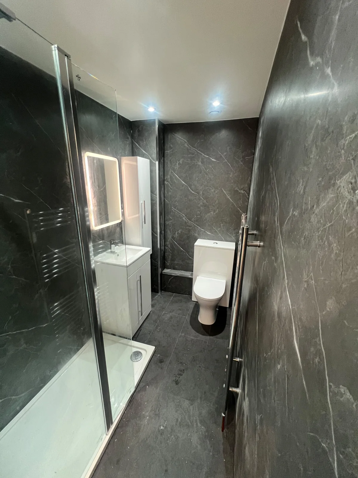 Dark marble-effect shower room with a white vanity and illuminated mirror