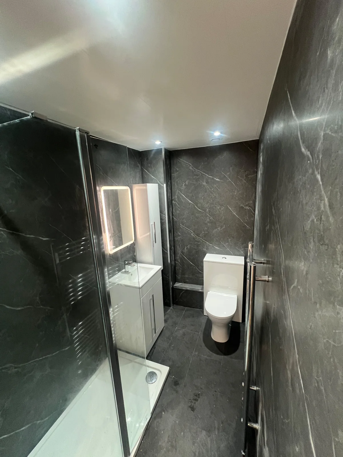 Glass shower screen and white fittings in a dark grey shower room