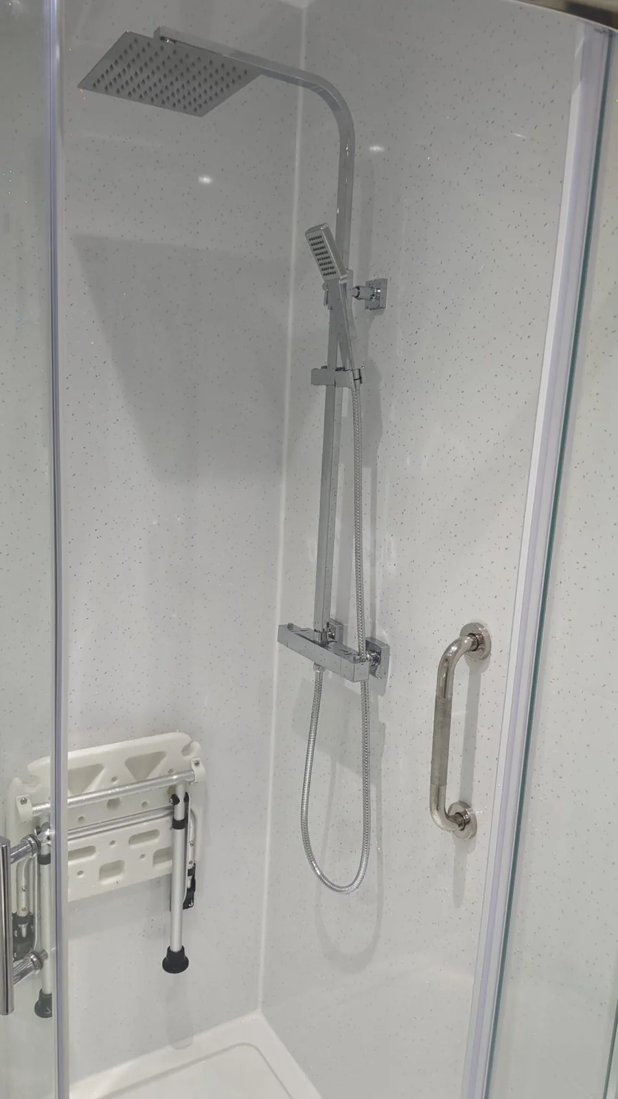 Chrome shower, grab rail and folding seat against white sparkle wall panels