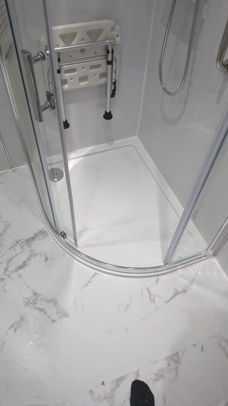 Curved glass shower enclosure with a white tray and marble-effect floor