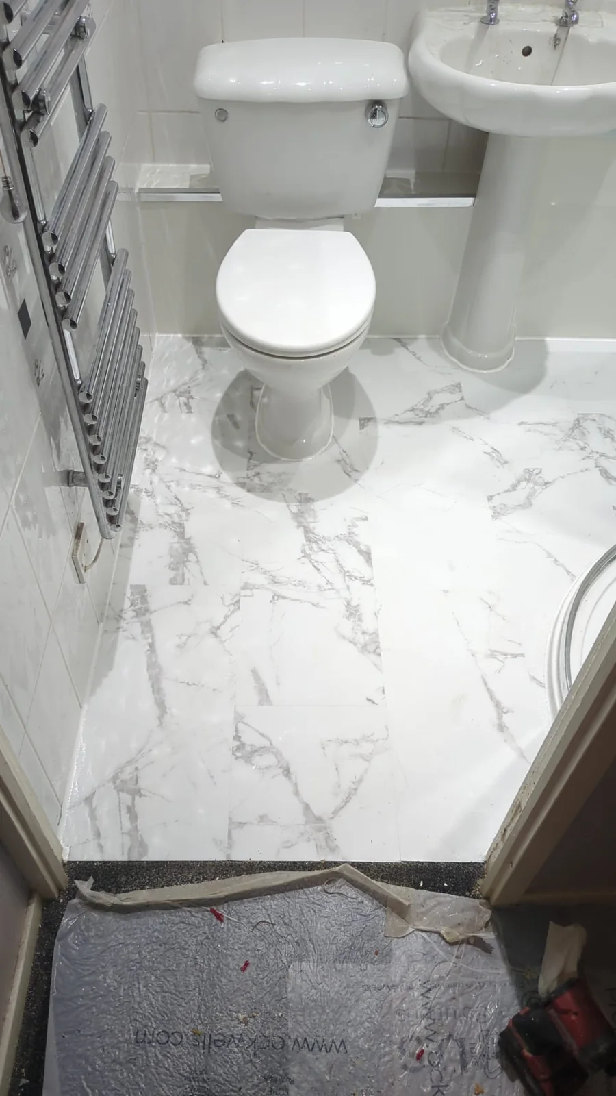 White toilet, pedestal basin and chrome towel radiator with marble-effect flooring