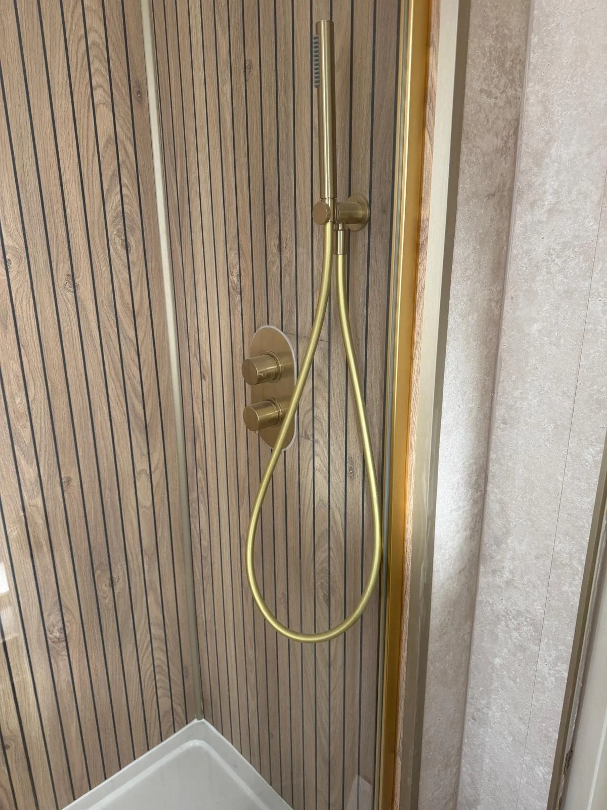 Gold handheld shower and controls beside wood-effect slatted wall panels