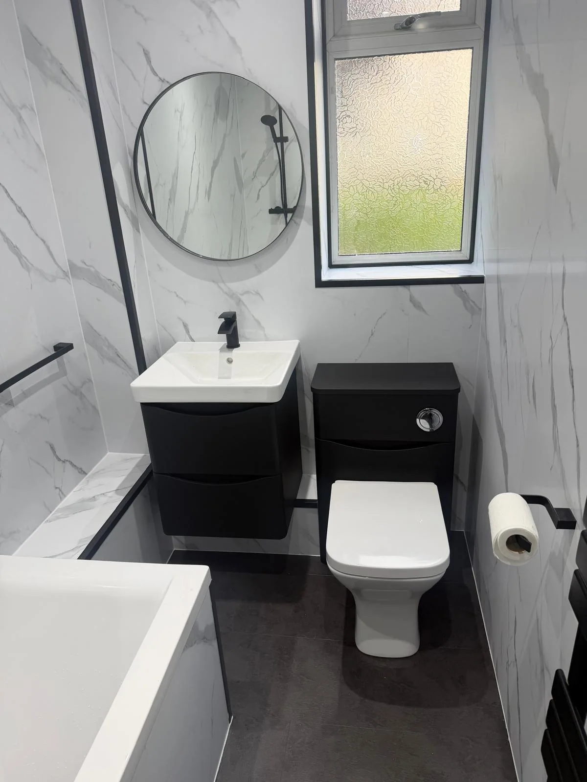 Black bathroom vanity and toilet unit with a round mirror and white marble-effect walls