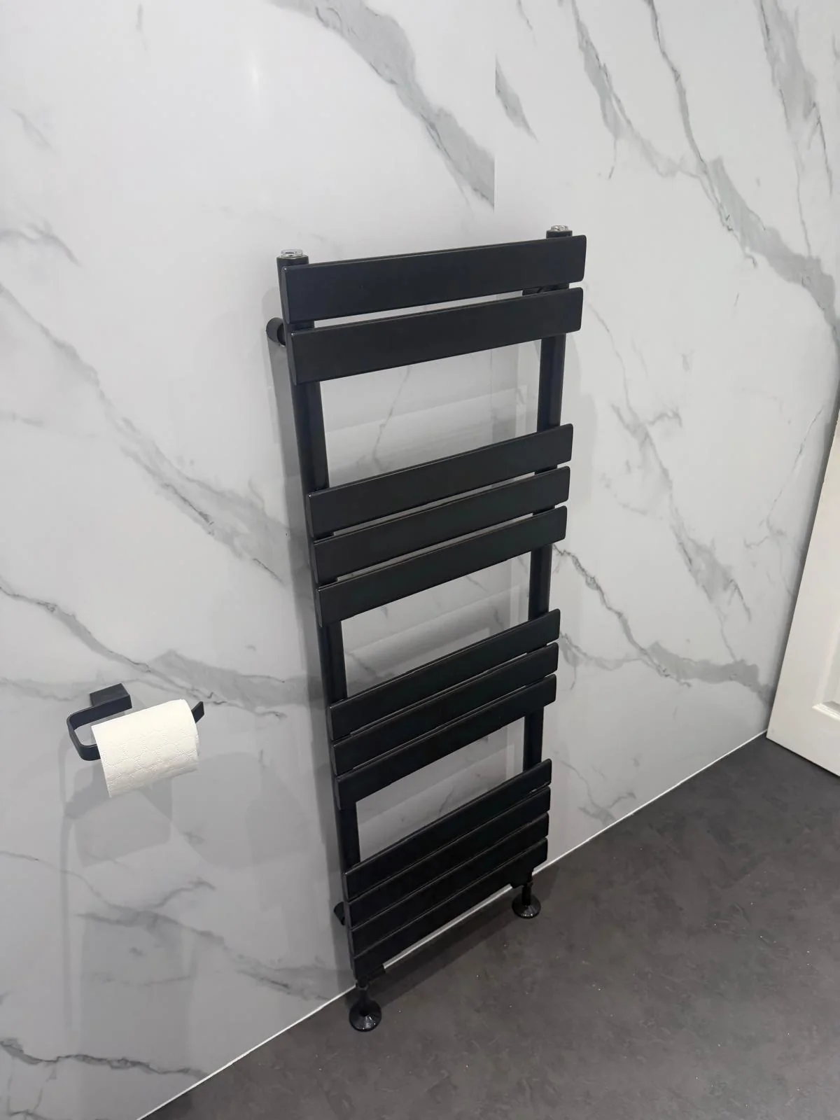Black heated towel radiator against white marble-effect wall panels