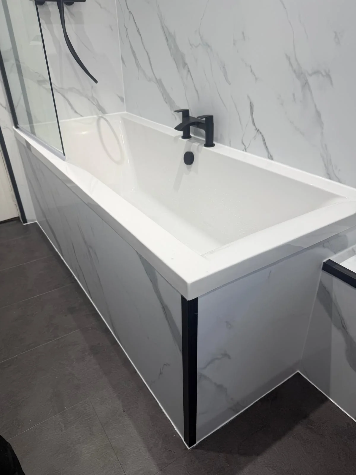 White fitted bath with a black mixer tap and marble-effect bath panel