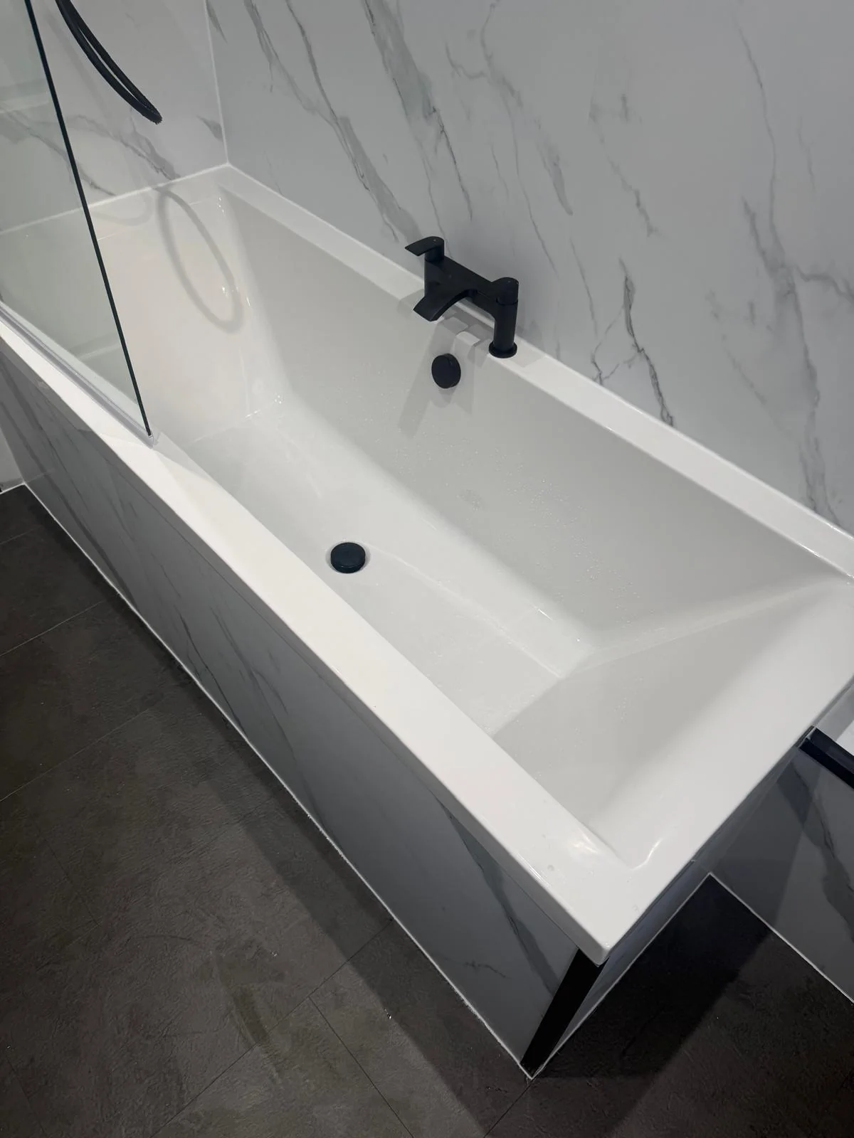White bath with black tap, waste and glass shower screen