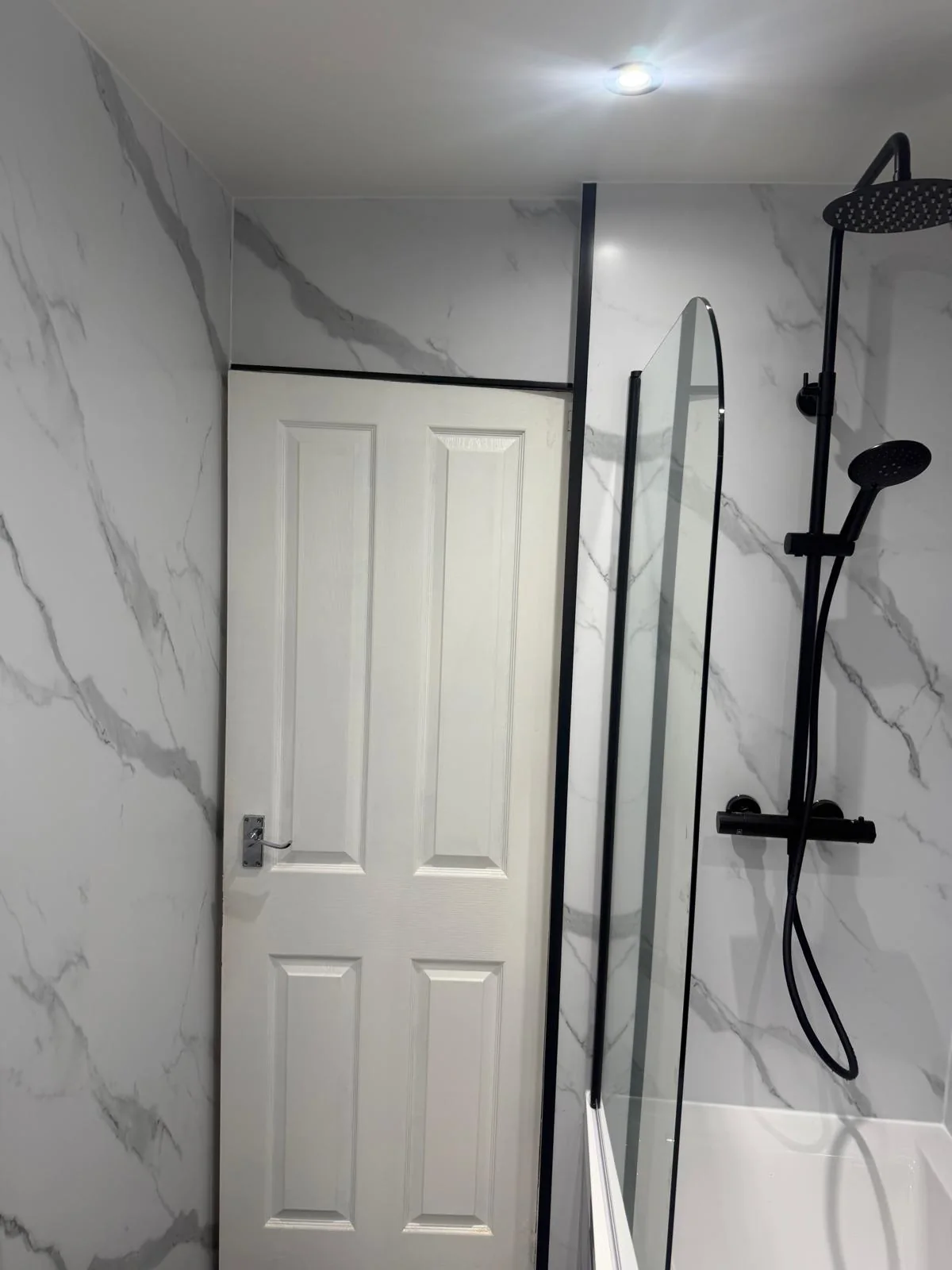Black shower fittings and glass bath screen beside a white bathroom door