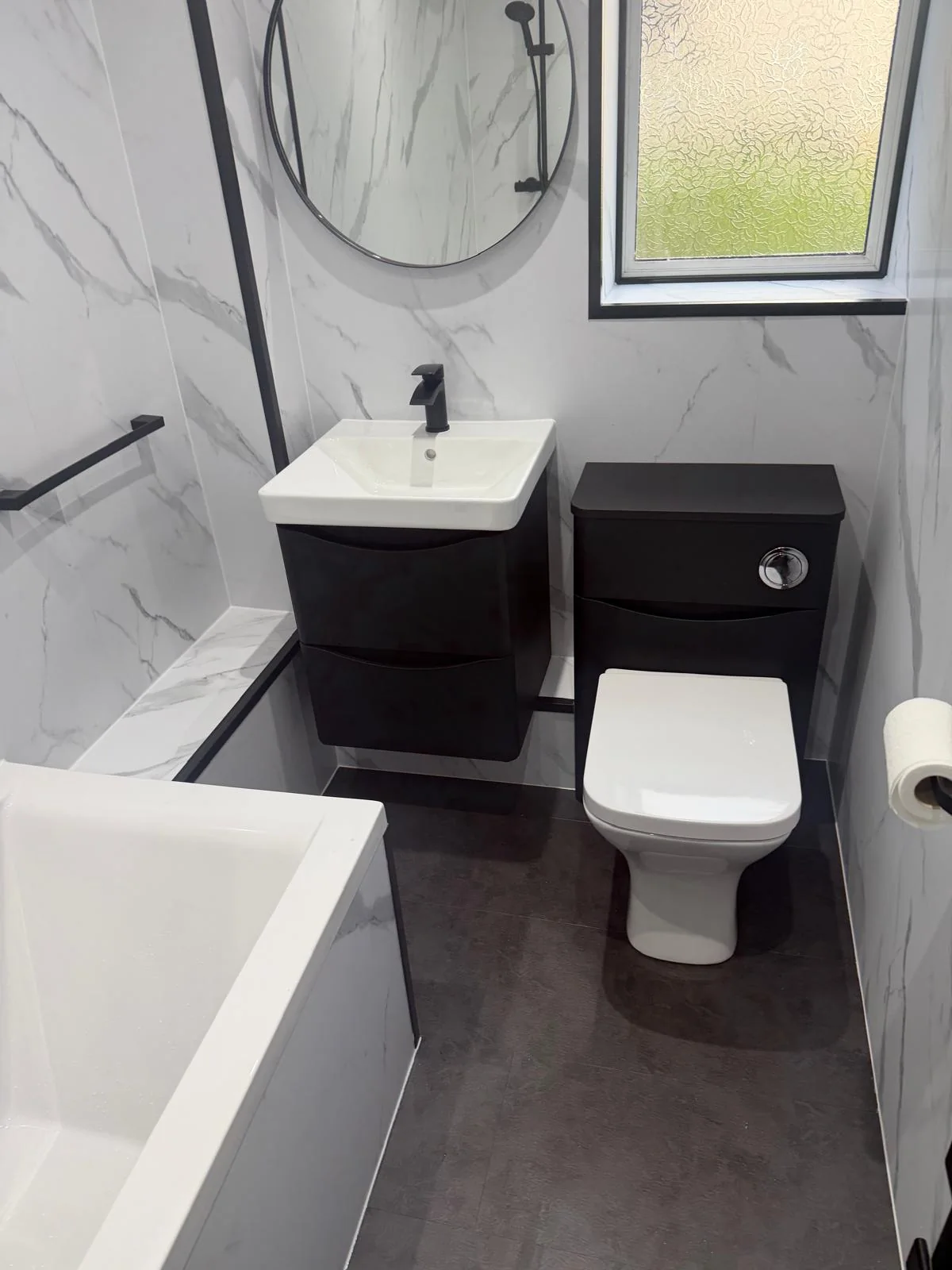 Black vanity drawers and toilet unit beneath a round bathroom mirror