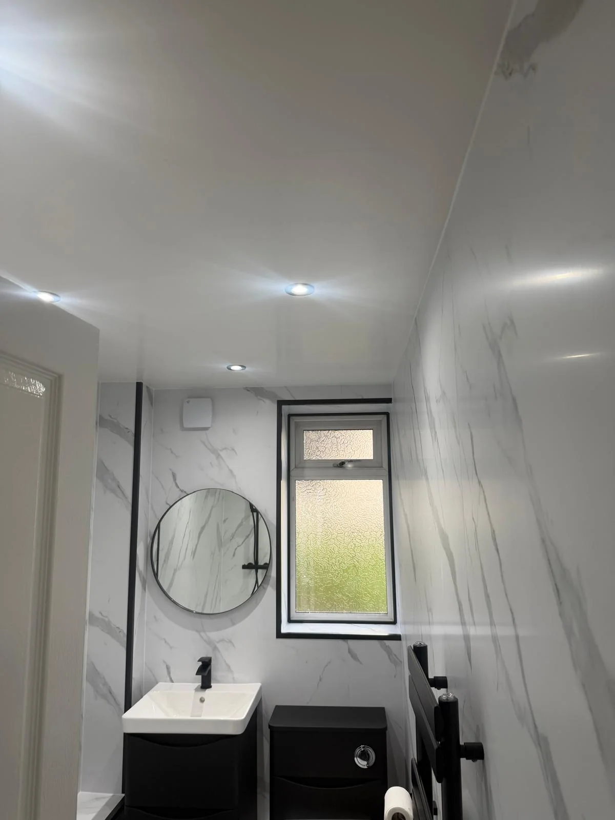 Recessed ceiling lights above black vanity storage and a round mirror