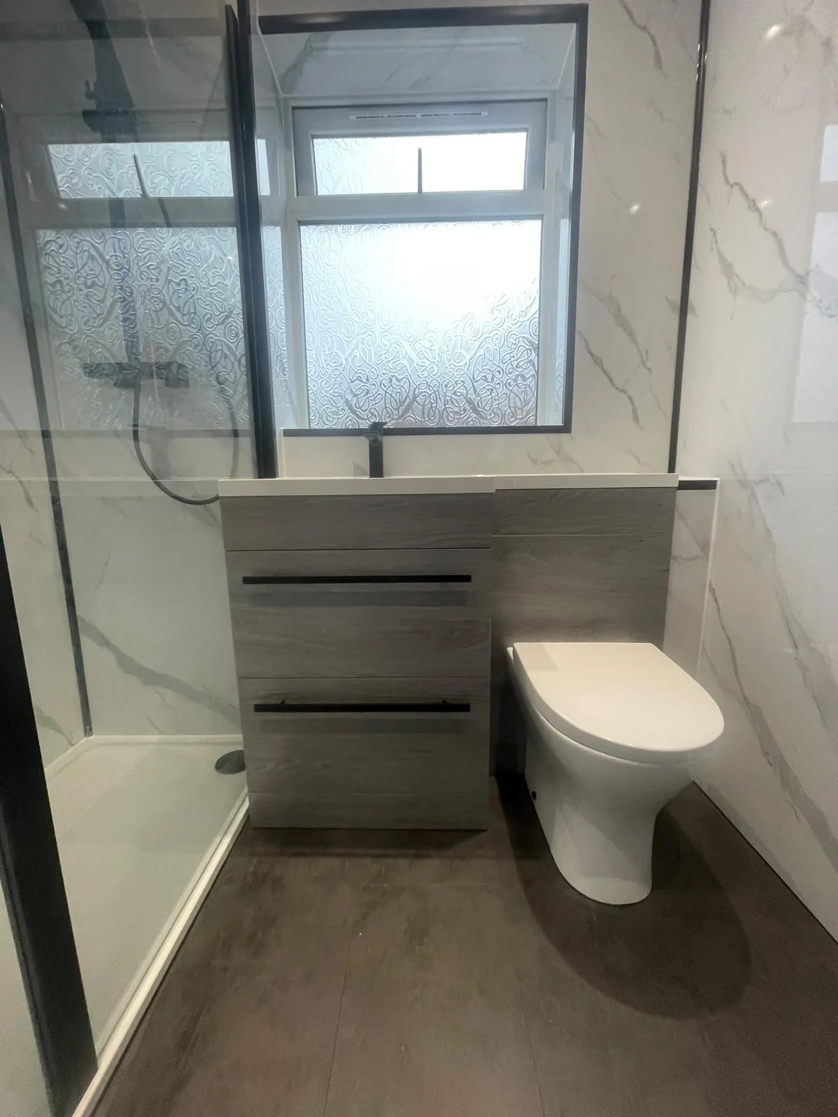 Grey wood-effect basin and toilet unit beside a glass shower enclosure