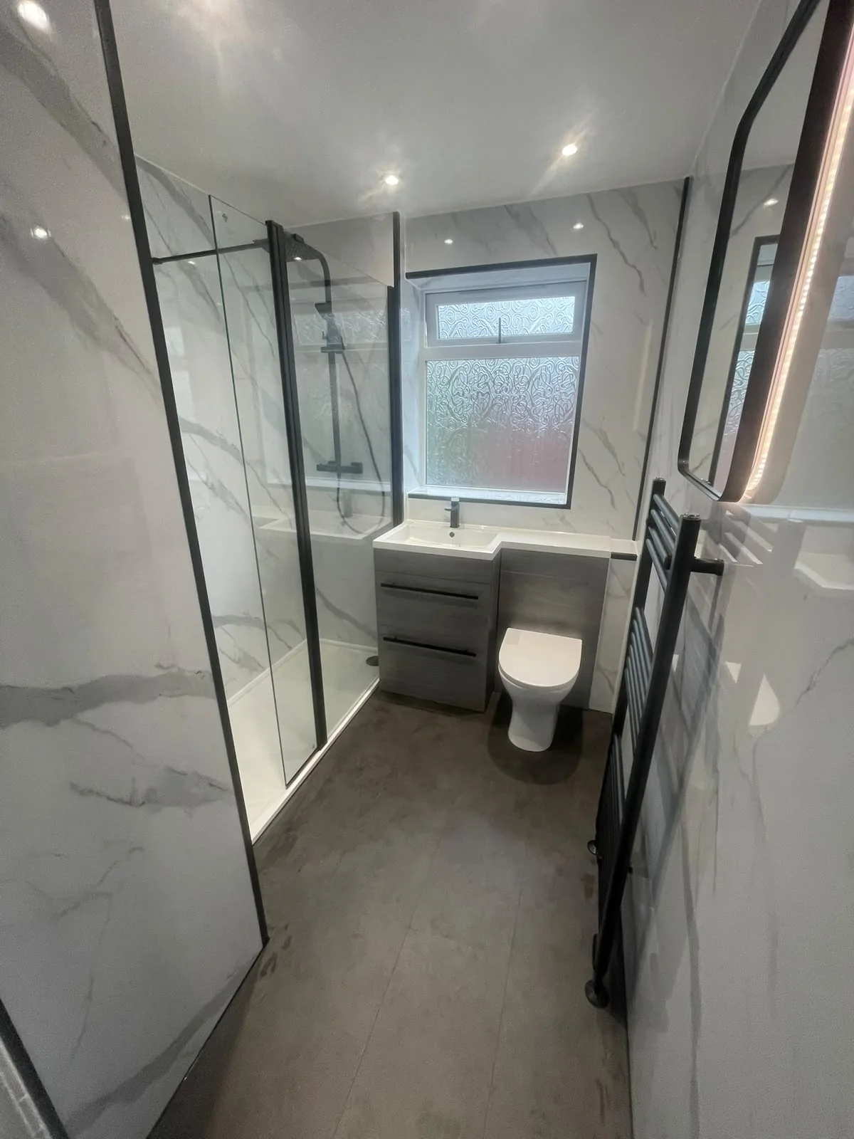 Black-framed shower and grey vanity beneath a frosted bathroom window