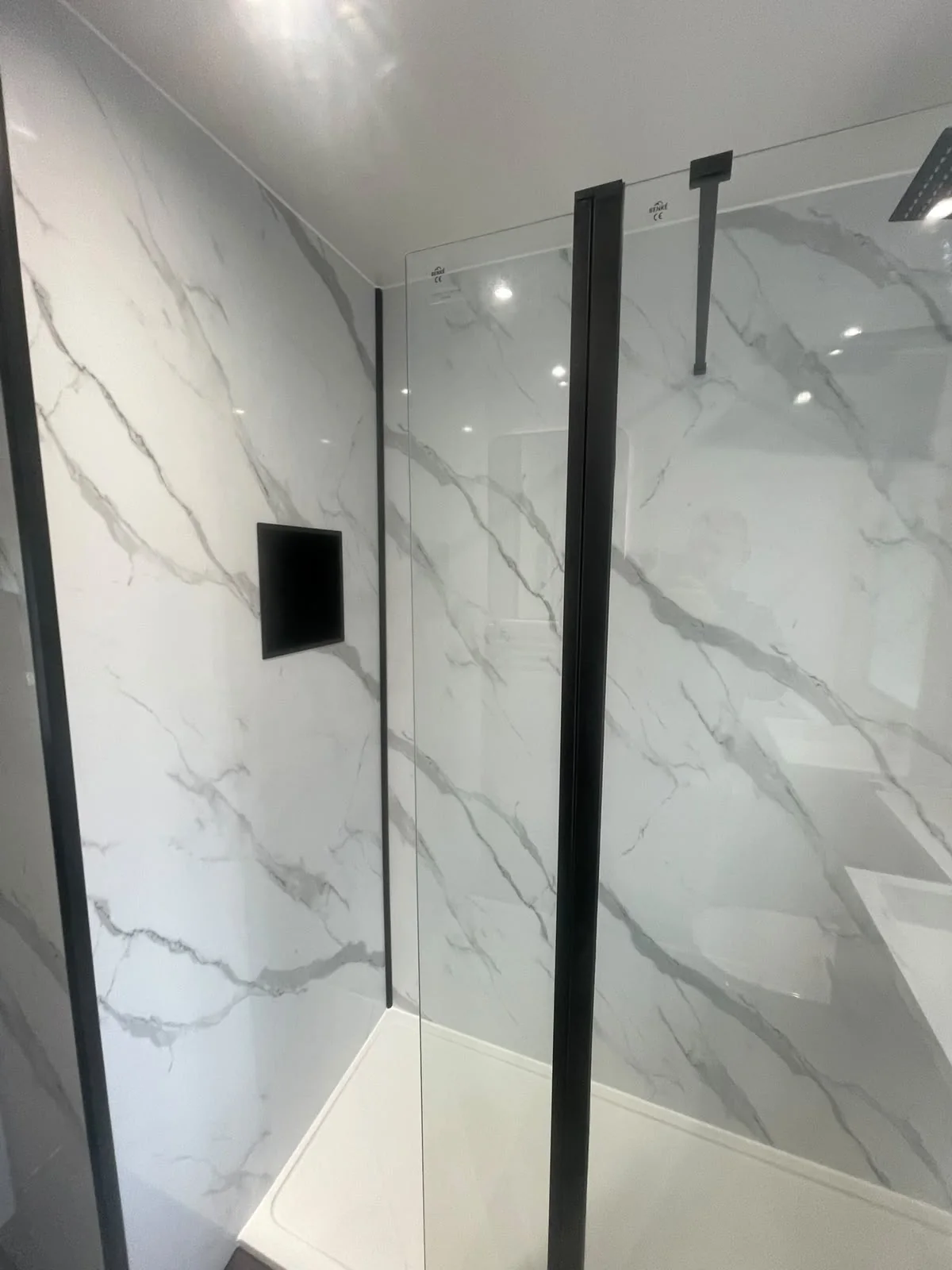 Black shower niche and glass screen against marble-effect wall panels