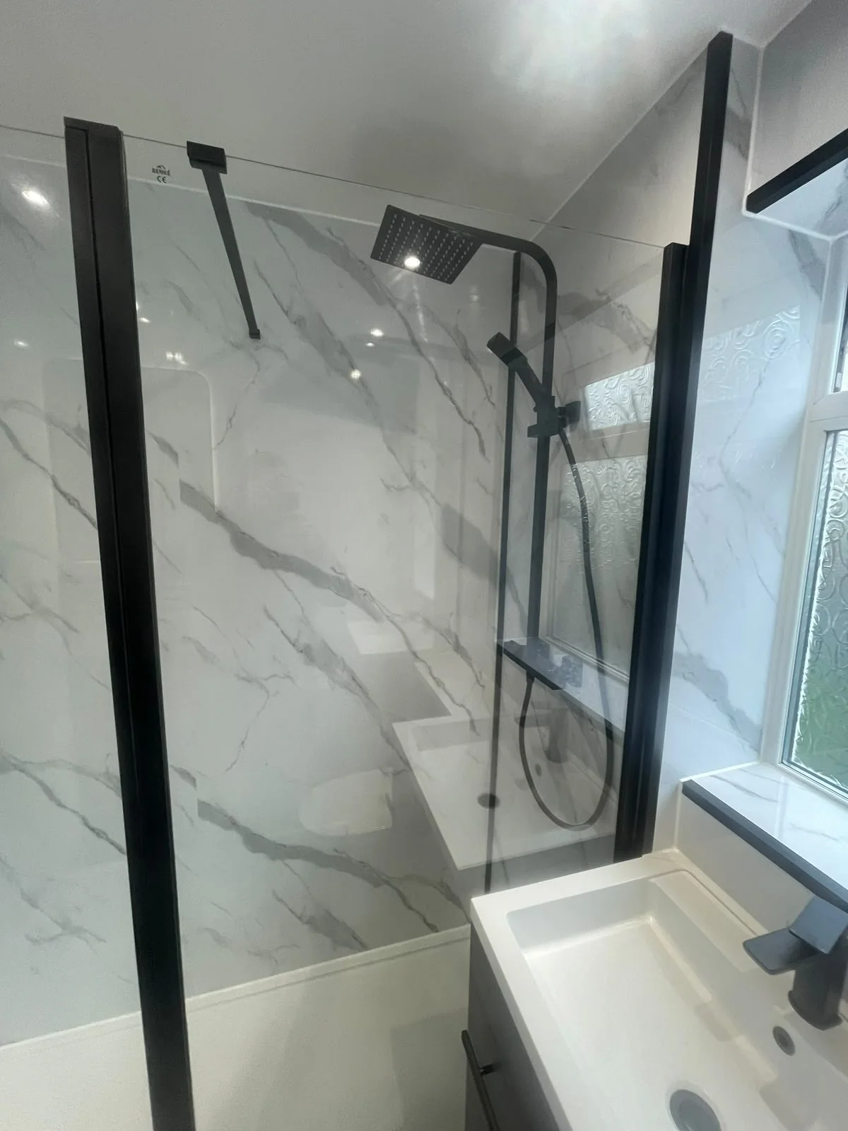 Black shower fittings behind a glass screen beside a white basin